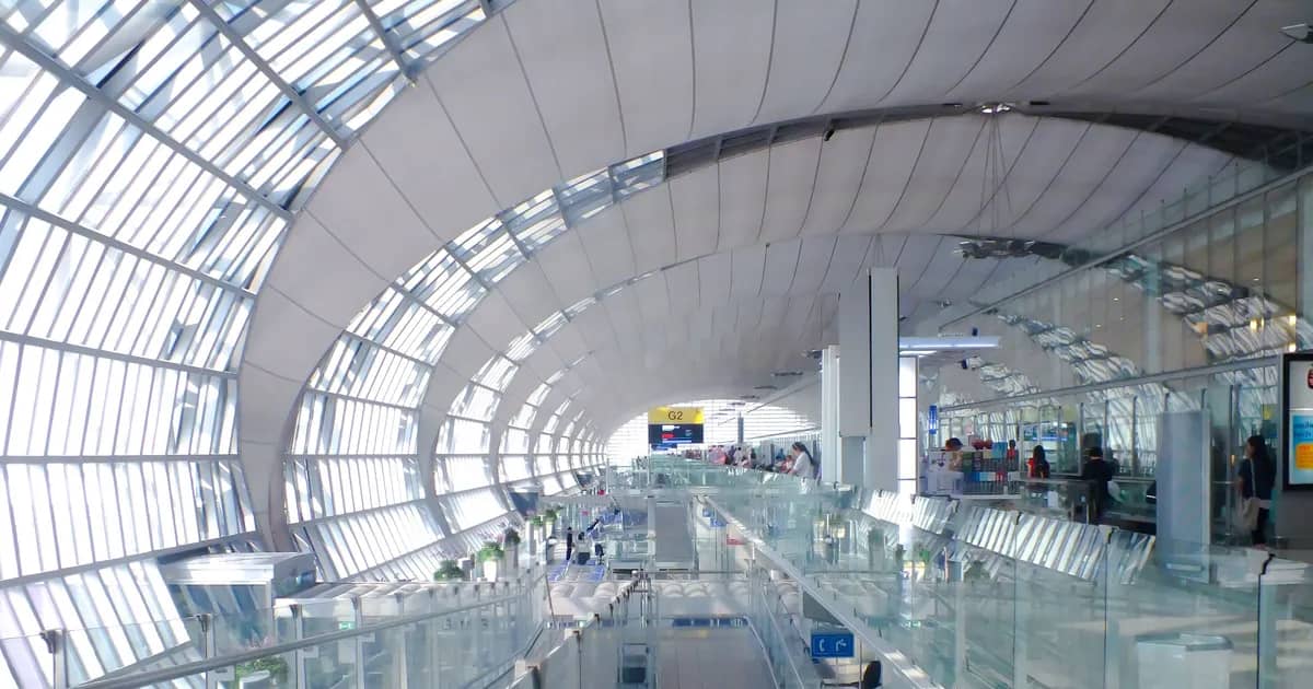 A long, light-filled airport terminal concourse under a curved glass and steel roof