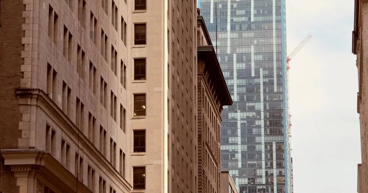 A historic stone office building standing against a modern glass tower in a financial district